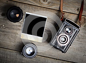 Vintage camera with lenses and blank old photograph on wooden background