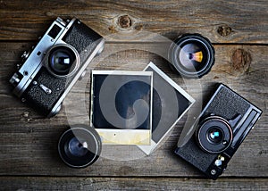 Vintage cameras with lenses and blank old photograph on wooden background