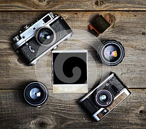 Vintage cameras with lenses and blank old photograph on wooden background