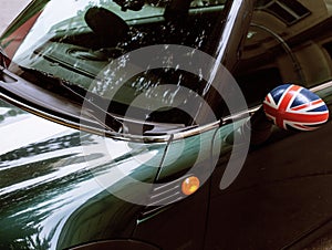 Vintage car detail, concept of British Patriotism shown as flag on mirror, trees in reflection windshield, body part