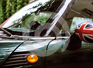 Vintage car detail, concept of British Patriotism shown as flag on mirror, trees in reflection windshield, body part