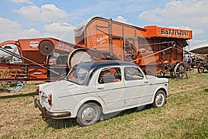Vintage car Fiat 1100 near to an old thresher machine