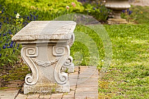 A vintage carved stone garden bench on grass field in a park or garden.