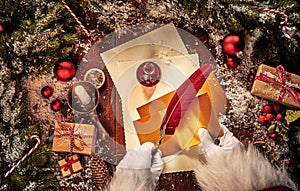 Vintage Christmas scene with Santa Claus writing a letter with a feather quill pen and decorations on a rustic table with