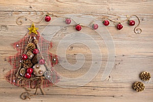 Vintage Christmas tree with burlap balls, cones, wooden sticks and red apples on beige wood background.