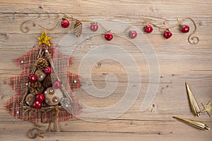 Vintage Christmas tree with burlap balls, cones, wooden sticks and red apples on beige wood background.