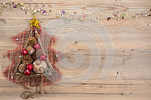Vintage Christmas tree with burlap balls, cones, wooden sticks and red apples on beige wood background.