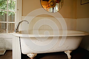 Vintage clawfoot cast iron bathtub in white and creme bathroom with wall decor and round mirror