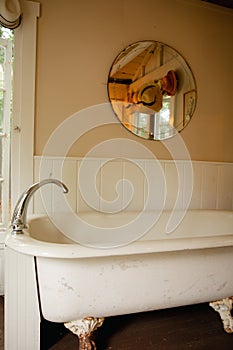 Vintage clawfoot cast iron bathtub in white and creme bathroom with wall decor and round mirror