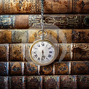 Vintage clock hanging on a chain on the background of old books. Old watch as a symbol of passing time. Concept on the theme of
