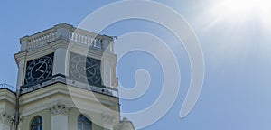 The vintage clock tower on facade of the residential building on blue sky background with sun glare. Urban backgrouund.