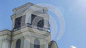 The vintage clock tower on facade of the residential building on blue sky background with sun glare. Urban backgrouund.