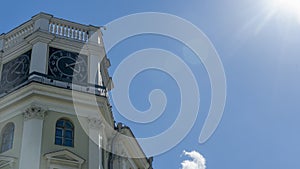 The vintage clock tower on facade of the residential building on blue sky background with sun glare. Urban backgrouund.