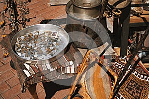 Vintage coins in a metal tray, rusty old cauldron and pots, key chains, rug and other goods in a shop at bazaar