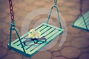 Vintage color tone style, glasses and white flower on the blue swing in evening