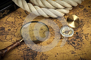 Vintage Compass and magnifying glass lies on an ancient world map - adventure stories background