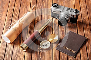 Vintage compass with spyglass, passport, map and photo camera on wooden table
