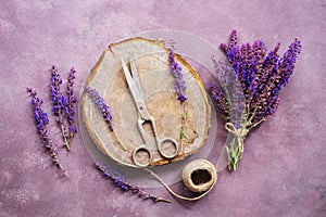 Vintage composition, bouquet of wild flowers of sage, plank stump, old scissors and a ball of thread on a purple rustic background