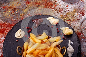 Vintage cooper bowl of french fries chips potato and sauces on black stone slate over rusty background. top view