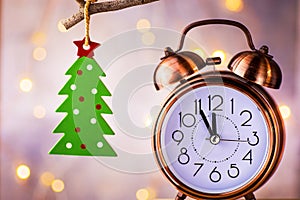 Vintage copper alarm clock showing five minutes to midnight, New Year countdown. Green christmas tree ornament hanging on branch