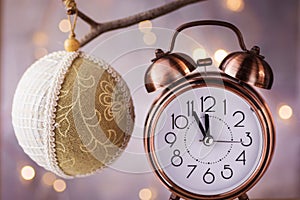 Vintage copper alarm clock showing five minutes to midnight, New Year countdown. Handmade linen fabric lace ball ornament hanging