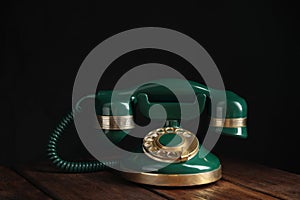 Vintage corded phone on wooden table against black background