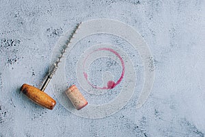 Vintage corkscrew, cork and red wine stain over gray background copy space.