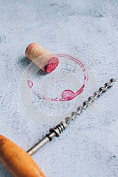 Vintage corkscrew, cork and red wine stain over gray background.