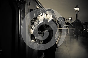 Vintage couple embracing and kissing on railway station platform as train is about to depart