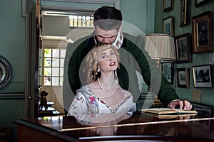 Vintage couple in period costume sitting around piano playing tunes with man kissing woman in the head