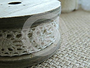Vintage cream lace on wooden bobbin on burlap background.