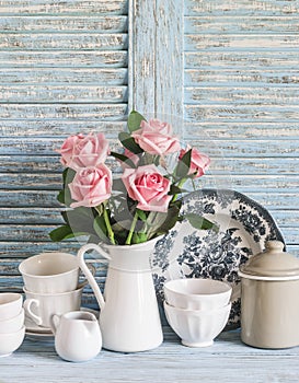 Vintage crockery in english style and rose bouquet on blue wooden rustic background. Kitchen still life in vintage country style.