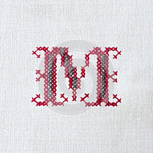 Vintage cross-stitch letter M on linen fabric