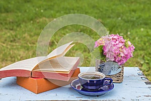 Vintage cup of coffee, open book and bouquet of hydrangea flowers in basket