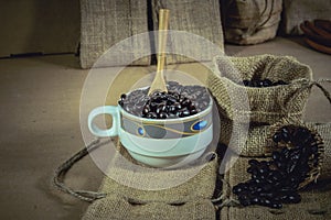 Vintage cup of roasted coffee beans on sack surface.