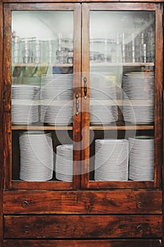 Vintage cupboard with dinnerware. old wooden kitchen cabinet with stack of white plates and cups. retro sideboard