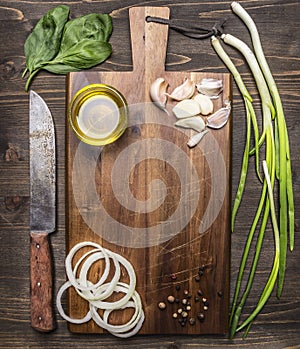 Vintage cutting board with ingredients for cooking, garlic, onion rings, green onions Oil knife place for text,frame on wooden