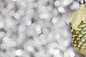 Vintage decorative christmas bauble in a shape of a pine cone in a green and yellow colors against silver blurry bokeh background