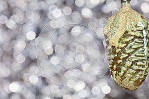 Vintage decorative christmas bauble in a shape of a pine cone in a green and yellow colors against silver blurry bokeh background