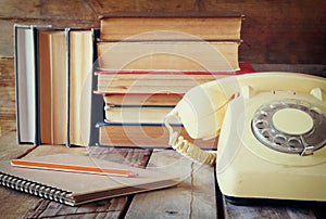 Vintage dial phone, phone book next to stack of old books over wooden table. vintage filtered image