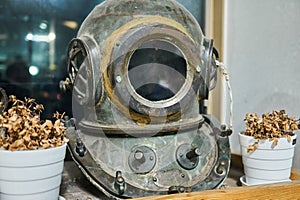 Vintage diving helmet displayed on a shelf with dry flowers on both sides.