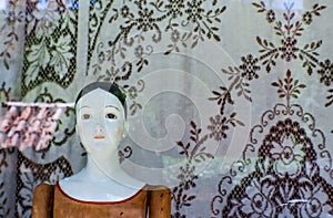 Vintage doll against old lace tablecloth in Santa Fe shop window with reflections of tile roof and the city