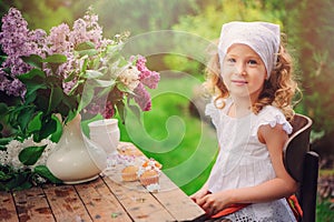 Vintage dressed child girl decorating cakes with flowers on garden tea party in spring