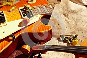 Vintage electric guitar, rare violin, dried flowers and old sheet music on wooden background closeup
