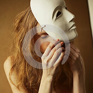 Vintage emotive portrait of a beautiful fashionable red-haired model with a white venetian mask - volto bianco. Close up. Retro photo