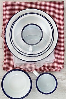 Vintage enamelware crockery on retro cloths on rustic wooden bac