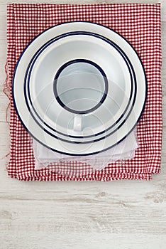 Vintage enamelware crockery on retro cloths on rustic wooden bac