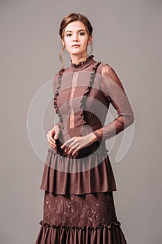 Vintage evening dress. Elegant brown gown. Brunette lady posing in studio