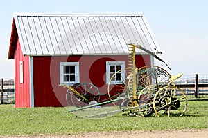 Vintage farm equipment in front of red building.