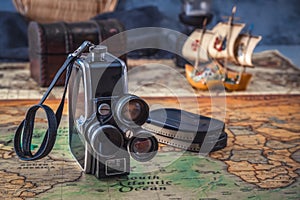 Vintage film camera with cassettes stands on an old nautical chart against the background of a wooden model of a sailboat.